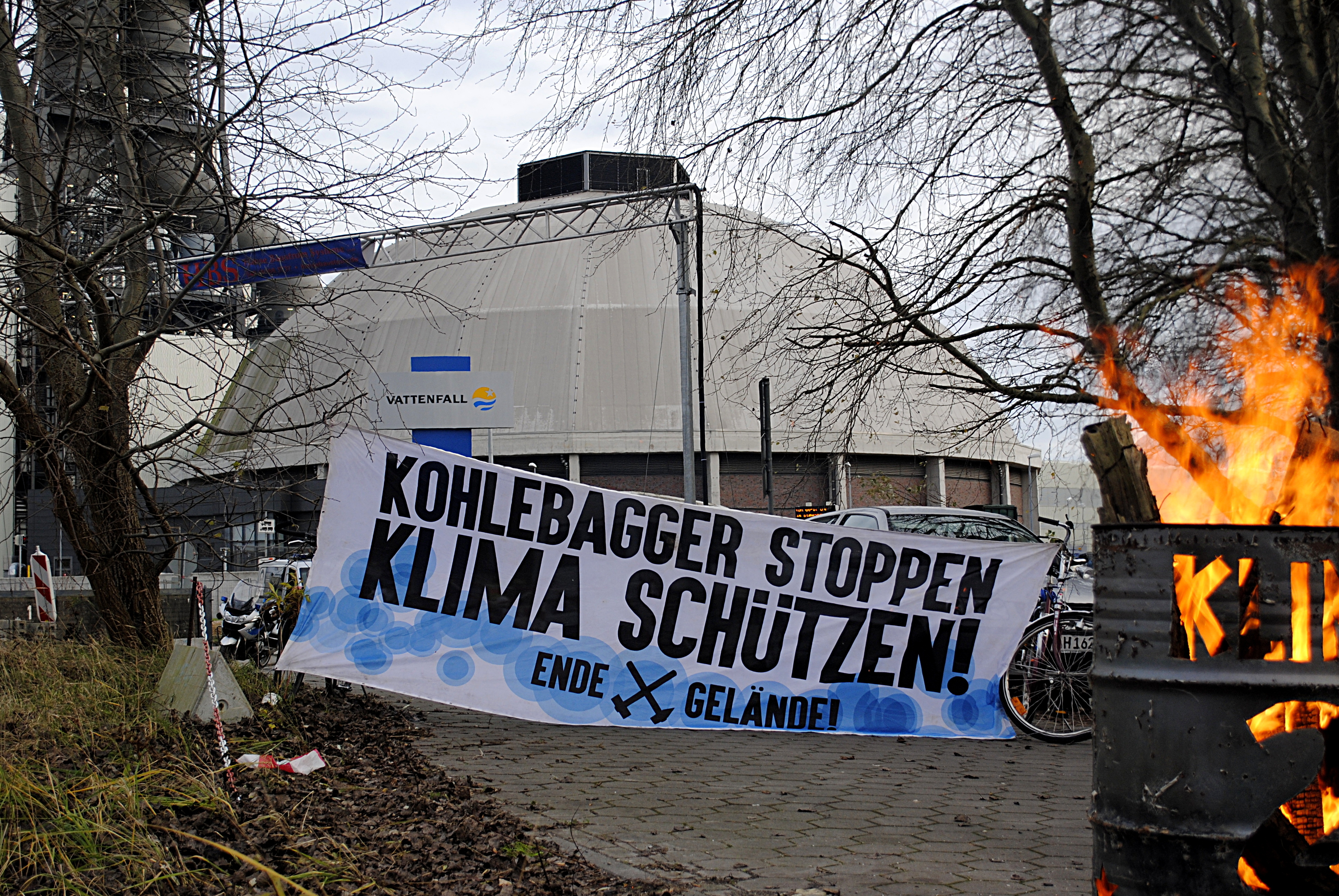 Feuertonne mit Transparent im Hintergrund: "Kohlebagger stoppen - Klima schützen! Ende Gelände"